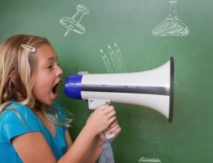 girl with a megaphone standing next to a chalkboard shouting into a megaphone