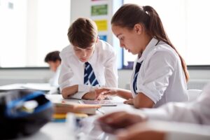 A boy and girl in school uniform working at a desk in a classroom