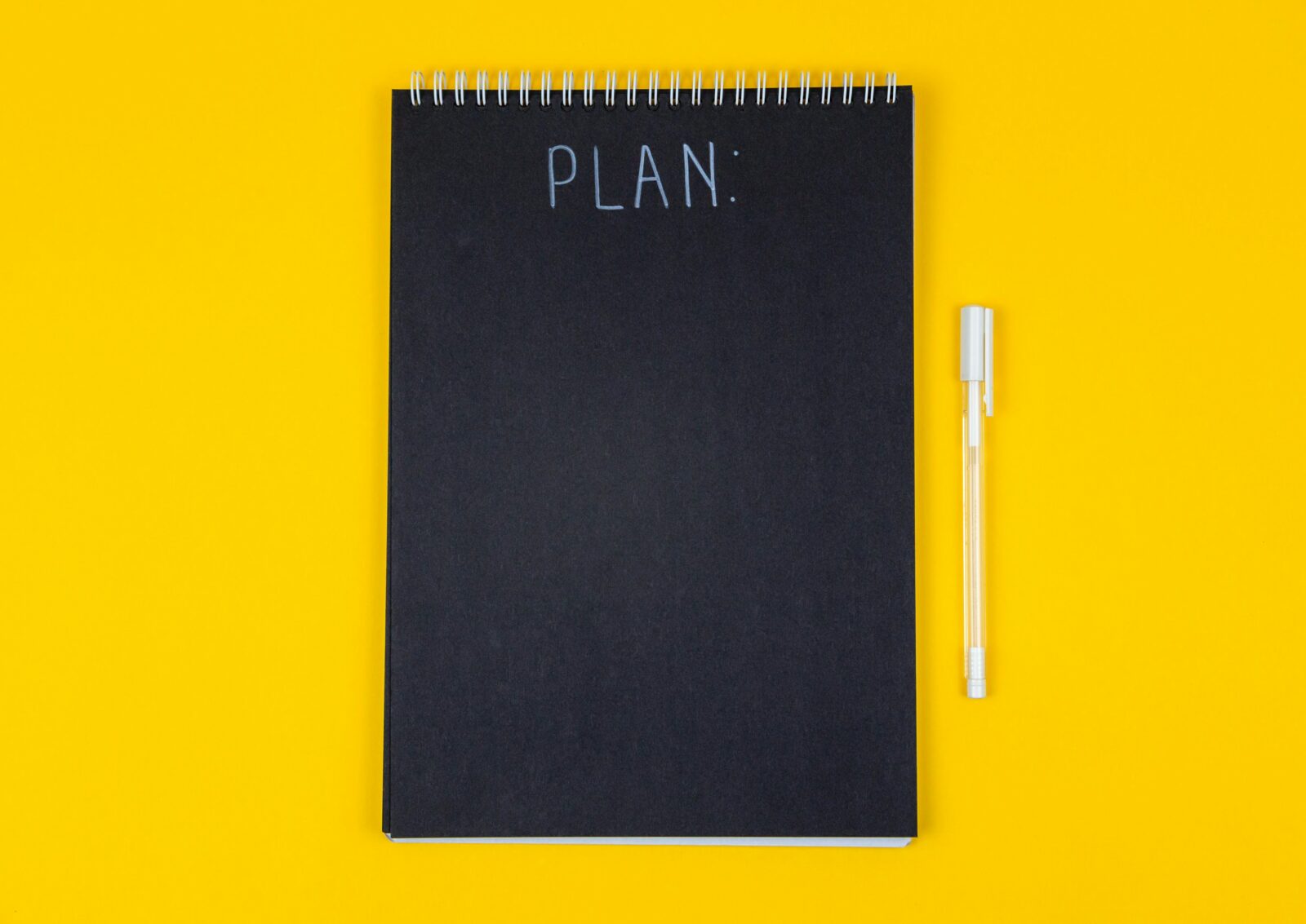 A black note book and white pen on a yellow background
